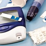 Blood glucose monitor with testing strips and a lancing device on a blue background