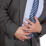 Man clutching stomach in pain, wearing a suit.