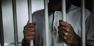 Person holding jail cell bars tightly.