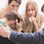 Group comforting a distressed person with hand on shoulder.