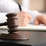 Judges gavel on desk with person writing.