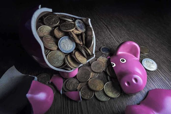 A broken pink piggy bank with coins spilling out onto a wooden surface
