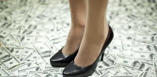 A pair of black high heels standing on a floor covered with dollar bills