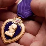 A hand holding a Purple Heart medal with a purple ribbon