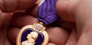 A hand holding a Purple Heart medal with a purple ribbon