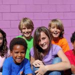 A group of six children smiling together in front of a purple wall