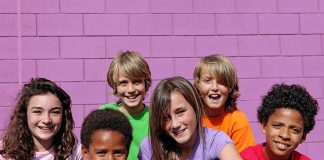 A group of six children smiling together in front of a purple wall