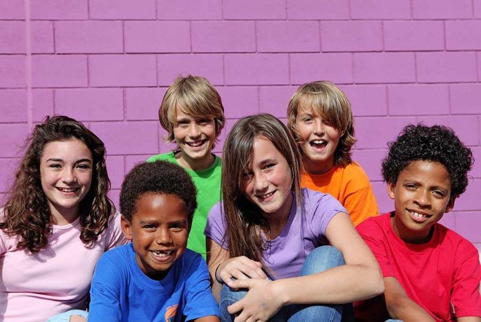 A group of six children smiling together in front of a purple wall