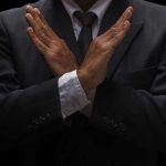 A man in a suit crossing his arms in a gesture of refusal or rejection