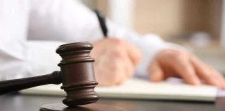 Judges gavel on desk with person writing.