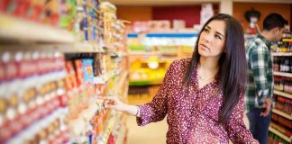 Woman shopping in a grocery store aisle with a cart full of vegetables