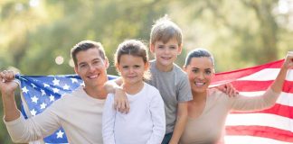 A family of four posing outdoors with an American flag