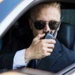 Man in suit using walkie-talkie in car.