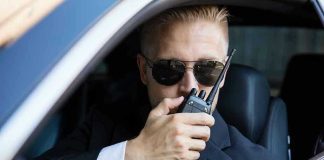 Man in suit using walkie-talkie in car.