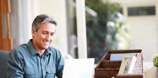 A man sitting at a desk working on a laptop with a smile