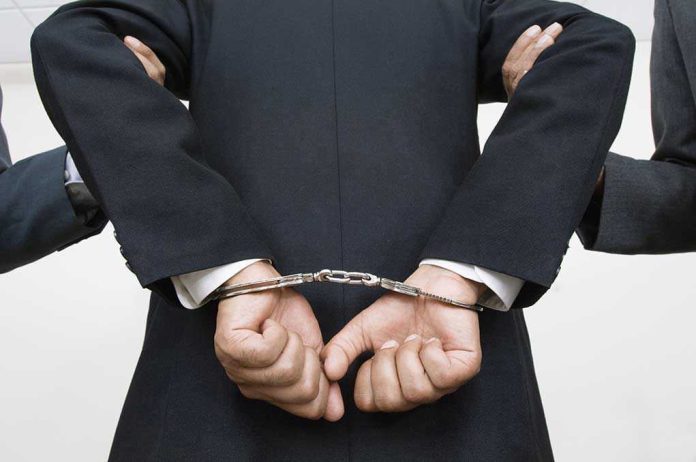 Person handcuffed in suit, escorted by two others.