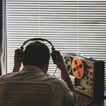 Person wearing headphones listening to a reel-to-reel tape recorder