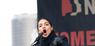 AOC Blasts Greene: Bigot Showdown! Woman speaking passionately at podium during outdoor event.