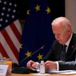 Biden Tapes Bombshell: 70 Hours Kept Secret Man seated at table with flags in background.