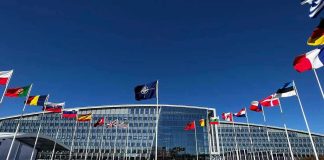 NATO Left Hanging: U.S. Strategic Cuts Unveiled Flags outside NATO headquarters building under clear blue sky.