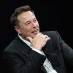 Trump’s China Power Move: Musk, Cook Lead Charge Man in suit smiling, resting chin on hand.