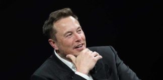 Man in suit smiling, resting chin on hand.