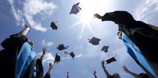 Graduating students celebrating by throwing their caps into the air under a bright blue sky