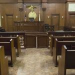 Justice Quits! What Did She Hide? Interior view of an empty courtroom with wooden benches and a judges bench