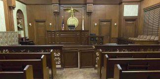 Justice Quits! What Did She Hide? Interior view of an empty courtroom with wooden benches and a judges bench
