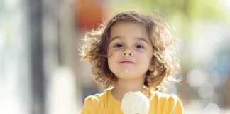 A young child with curly hair holding an ice cream cone outdoors