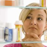 Menstrual Pay Fight Explodes — What’s Next? A woman thoughtfully looking at a medicine cabinet filled with various medications
