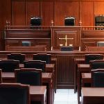Empty courtroom with wooden furniture and black chairs.