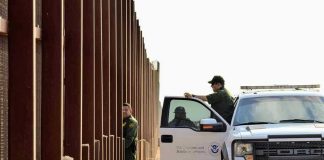 Cartel Super Tunnel Found Under San Diego Border patrol agents near a tall metal fence.
