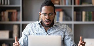 Blame Game Explodes Over Black America Man surprised while looking at laptop screen.