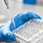 Taxpayer-Funded Biolabs Exposed — 120+ Worldwide Gloved hand pipetting liquid into a tray.