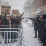 Protesters holding signs against ICE in a snowy environment
