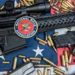 A rifle and handgun surrounded by ammunition on an American flag