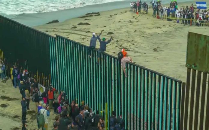 shutterstock_1229072278 People climbing a tall beachside border fence