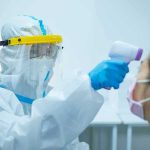 Healthcare worker in PPE checks patient temperature with infrared thermometer