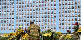Soldier kneels before memorial wall with photos and flowers