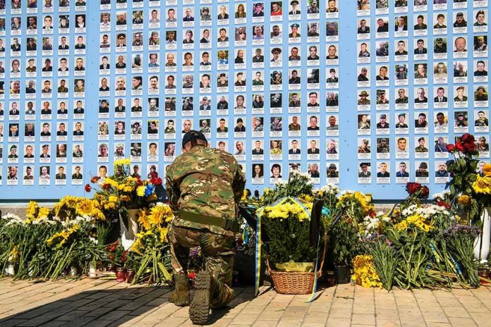 shutterstock_1808747695 Soldier kneels before memorial wall with photos and flowers