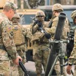 Soldiers in camouflage gather around a mortar during field training