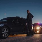 Police officer stands beside a stopped car at dusk