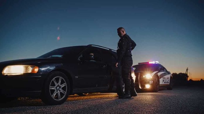 shutterstock_2232055275 Police officer stands beside a stopped car at dusk