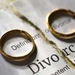 Two wedding rings placed on a torn page with the word 'Divorce'