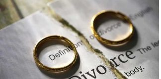 Two wedding rings placed on a torn page with the word 'Divorce'