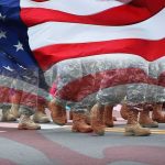American flag overlay on marching soldiers' boots in formation
