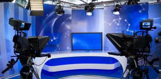 Prison To Primetime—George Santos Tests Limits A television studio setup with cameras and a blue backdrop