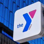 Girls’ Spaces Threat? YMCA Retreats YMCA sign mounted on a modern glass building