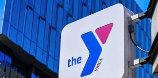 Girls’ Spaces Threat? YMCA Retreats YMCA sign mounted on a modern glass building